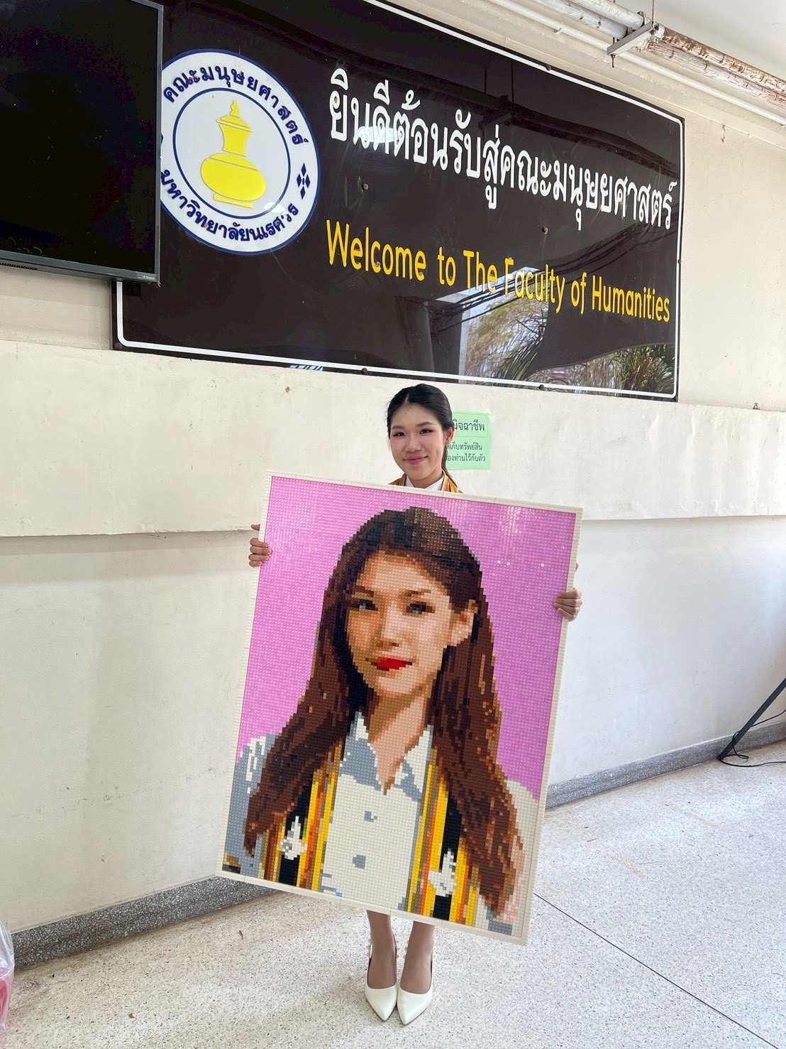 บัณฑิตถือภาพโมเสกพอร์ตเทรตหน้าป้ายคณะมนุษยศาสตร์